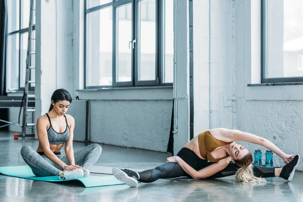 Chicas deportivas multirraciales estirándose en colchonetas de yoga en el gimnasio — Stock Photo