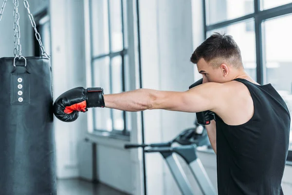 Vista laterale di muscoloso giovane pugilato con sacco da boxe in palestra — Foto stock