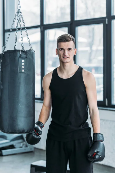 Guapo hombre deportivo en guantes de boxeo sonriendo a la cámara en el gimnasio - foto de stock