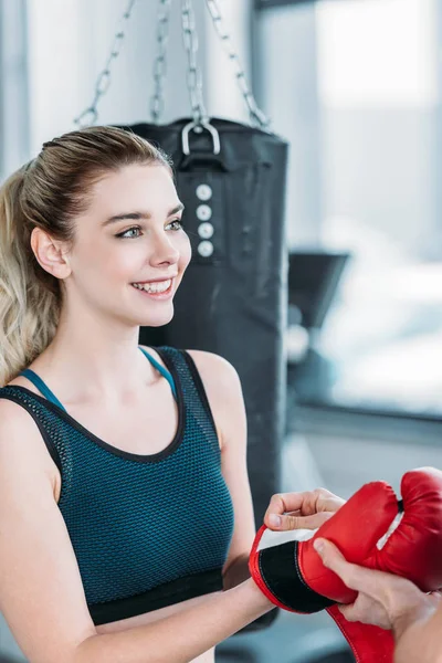 Lächelnde junge Sportlerin mit Boxhandschuhen und wegschauendem Blick im Fitnessstudio — Stockfoto