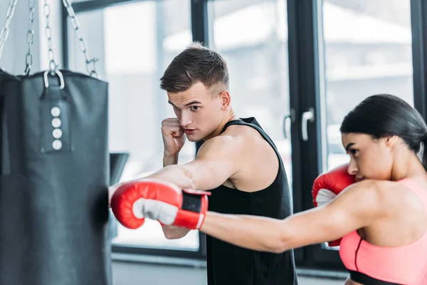 Male trainer and african american girl boxing with punching bag in gym — Stock Photo