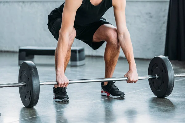 Обрезанный кадр мускулистого молодого человека в спортивной одежде, поднимающего штангу в спортзале — стоковое фото