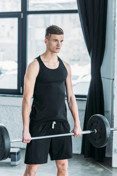 Jovem atleta concentrado levantando barbell e olhando para longe no ginásio — Fotografia de Stock