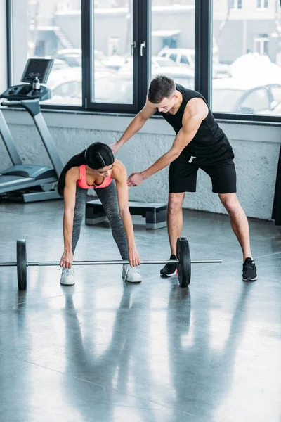 Entraîneur masculin aidant sportive afro-américaine fille levant haltère dans la salle de gym — Photo de stock