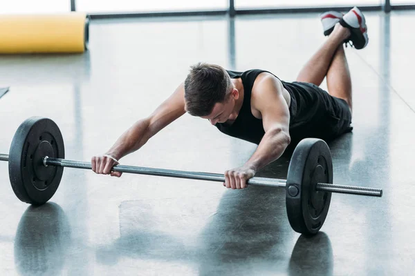 Sporty yougn hombre mintiendo y entrenamiento con barbell en gimnasio - foto de stock