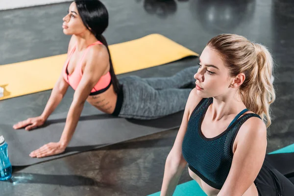 Vista de ángulo alto de hermosas chicas deportivas multiétnicas ejercitándose en colchonetas de yoga en el gimnasio - foto de stock