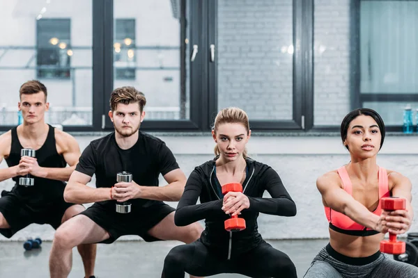 Sporty young men and women doing sit ups with dumbbells in gym — Stock Photo