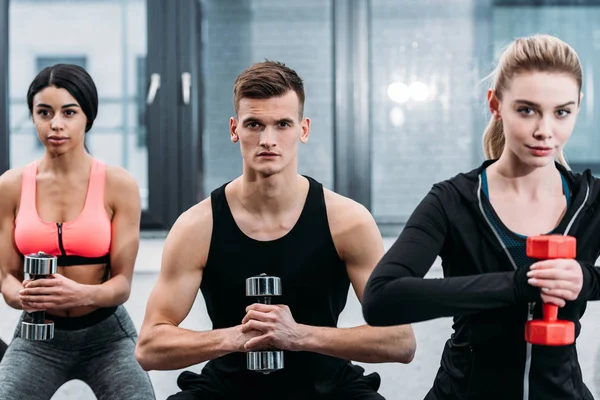 Muscular young people training with dumbbells and looking at camera in gym — Stock Photo