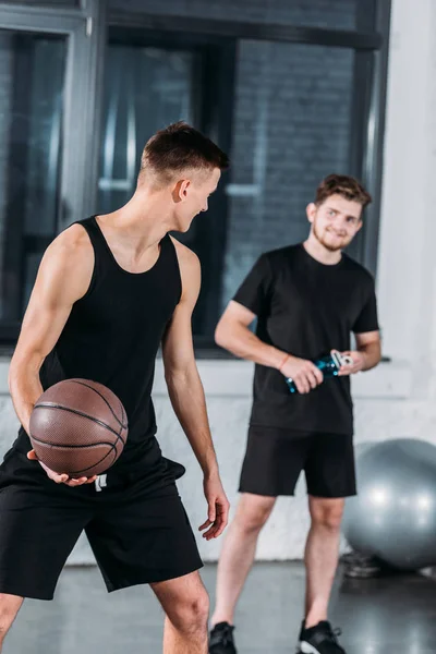 Улыбающиеся юноши в спортивной одежде играют в баскетбол в спортзале — стоковое фото