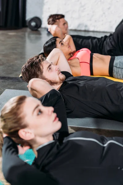 Deportistas jóvenes multirraciales tumbados en colchonetas de yoga y haciendo abdominales en el gimnasio - foto de stock