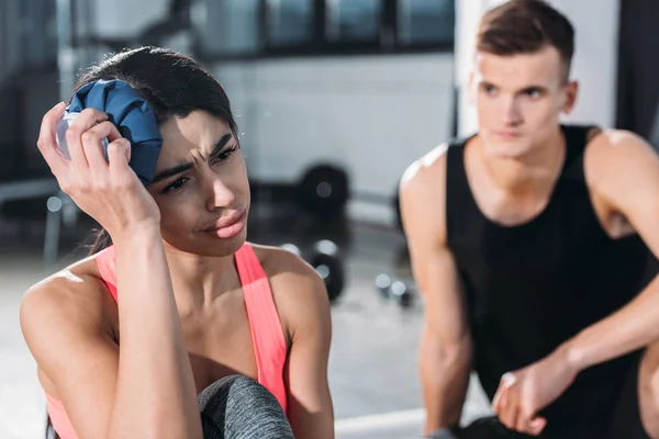 Joven afroamericana deportista sosteniendo bolsa de hielo en la cabeza y sufriendo de lesiones en el gimnasio - foto de stock