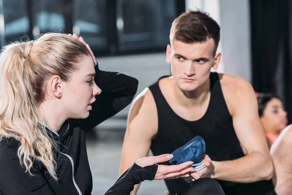 Young sportsman giving ice pack to upset sporty girl suffering from head injury in gym — Stock Photo