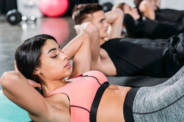 Jeunes sportifs multiethniques allongés sur des tapis de yoga et faisant des abdos dans la salle de gym — Photo de stock