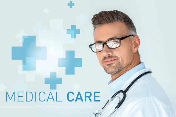 Porträt eines gut aussehenden Arztes mit Brille und Stethoskop auf den Schultern, der in die Kamera blickt, isoliert auf weiß mit medizinischem Versorgungsaufdruck — Stockfoto