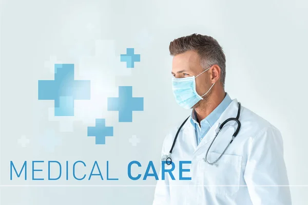 Bello medico in maschera medica guardando lontano isolato su bianco con iscrizione cure mediche — Foto stock