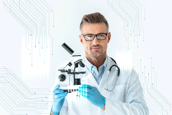 Bello scienziato in occhiali tenendo microscopio e guardando la fotocamera su bianco con interfaccia tecnologica — Foto stock
