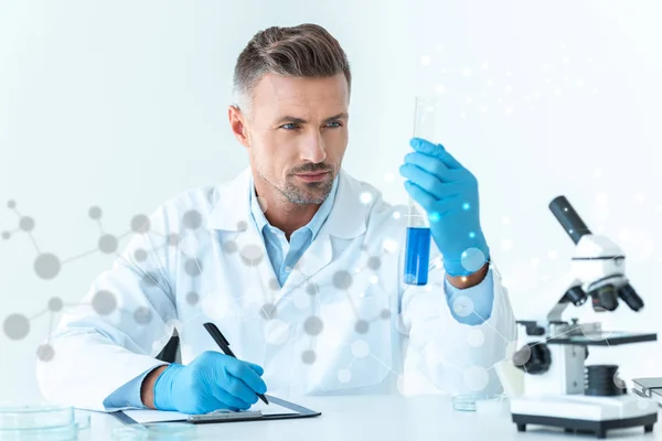 Bello scienziato guardando provetta con reagente blu — Foto stock