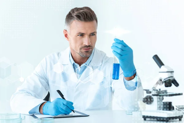 Handsome scientist looking at test tube with blue reagent — Stock Photo