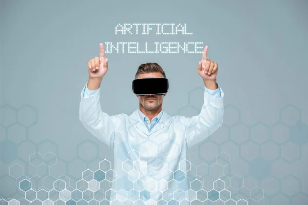 Scientist in virtual reality headset touching artificial intelligence lettering with two fingers isolated on grey — Stock Photo