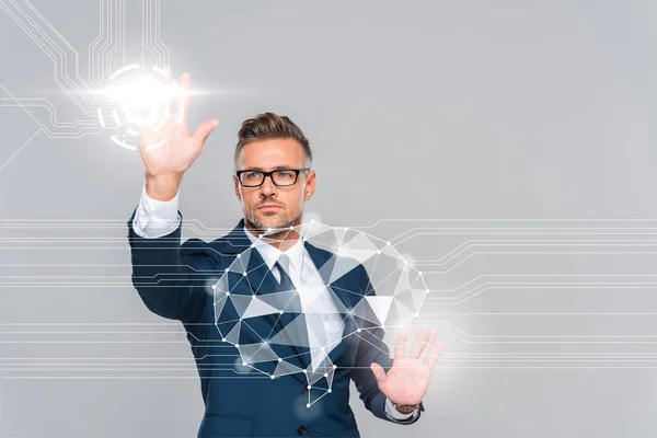 Hombre de negocios guapo en traje azul y gafas tocando cerebro aislado en gris, concepto de inteligencia artificial - foto de stock