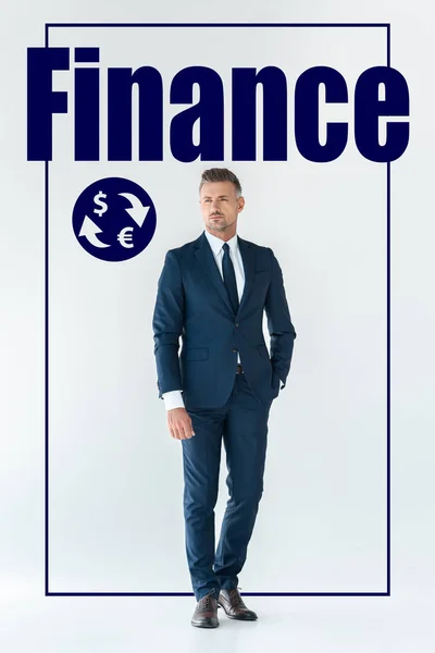 Guapo hombre de negocios en traje azul de pie y mirando hacia otro lado aislado en blanco con iconos financieros - foto de stock