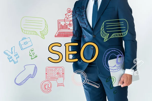 Sección media del hombre de negocios de pie con el ordenador portátil aislado en blanco con iconos seo - foto de stock