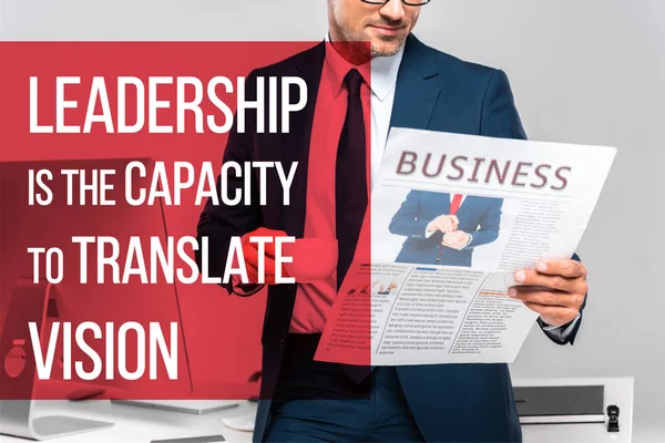 Cropped image of businessman holding cup of coffee and reading business newspaper isolated on grey with leadership lettering — Stock Photo