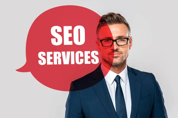 Portrait of handsome businessman in suit and glasses looking at camera isolated on grey with seo services — Stock Photo