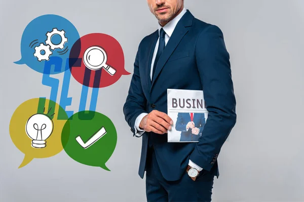 Abgeschnittenes Bild eines Geschäftsmannes, der Zeitung isoliert auf grau mit SEO-Symbolen hält — Stockfoto