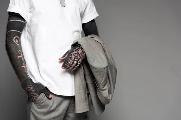 Cropped shot of tattooed man in white t-shirt holding suit jacket isolated on grey — Stock Photo