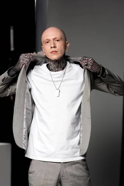 Guapo hombre tatuado elegante con chaqueta de traje y mirando a la cámara en el estudio - foto de stock