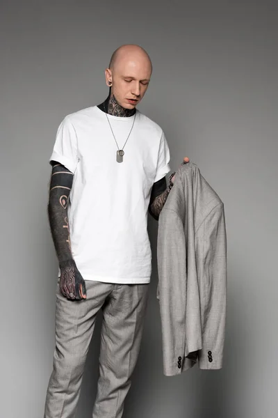 Стильный лысый татуированный мужчина, держащий пиджак на сером — стоковое фото