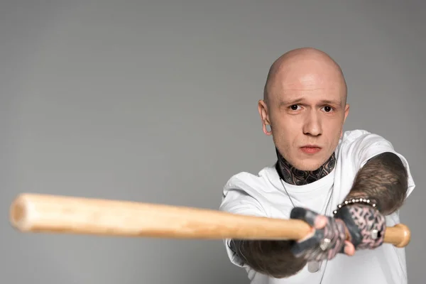 Serious tattooed man hitting with baseball bat and looking at camera isolated on grey — Stock Photo