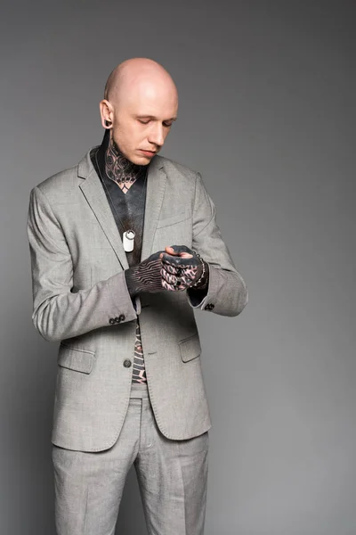 Stylish bald tattooed man in suit adjusting bracelet isolated on grey — Stock Photo