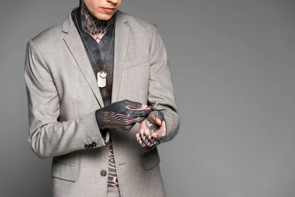 Cropped shot of stylish tattooed man adjusting bracelet isolated on grey — Stock Photo