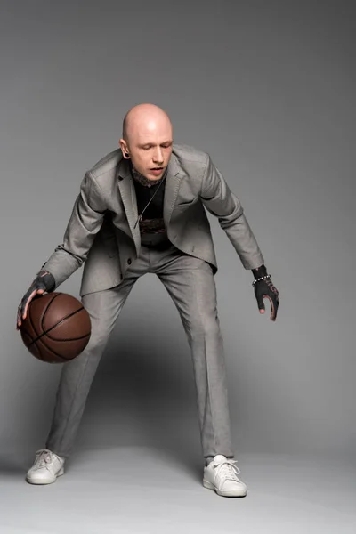 Vista completa de hombre tatuado con estilo en traje jugando baloncesto en gris - foto de stock