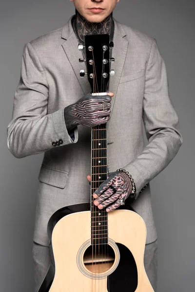 Cropped shot of tattooed man in suit holding acoustic guitar isolated on grey — Stock Photo