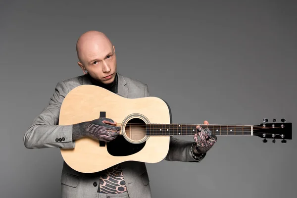 Handsome bald tattooed man in suit playing guitar and looking at camera isolated on grey — Stock Photo