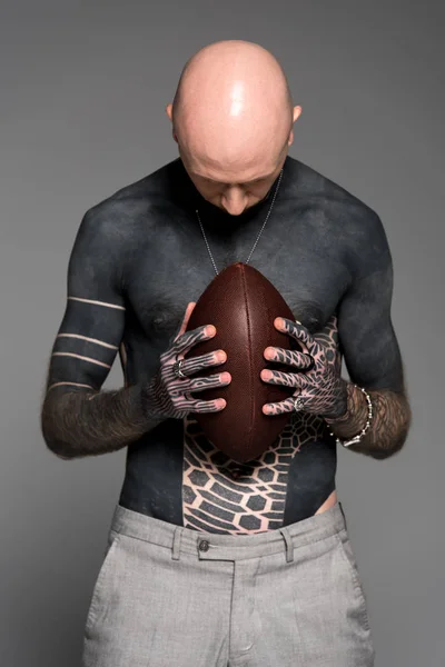 Calvo uomo tatuato senza maglietta che tiene la palla da rugby isolata sul grigio — Foto stock