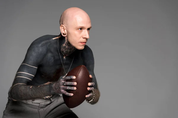 Concentrated bare-chested tattooed man holding rugby ball and looking away isolated on grey — Stock Photo