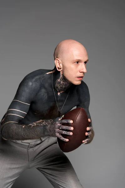 Konzentrierter, hemdloser Mann mit Tätowierungen, der einen Rugby-Ball in der Hand hält und isoliert auf grau blickt — Stockfoto