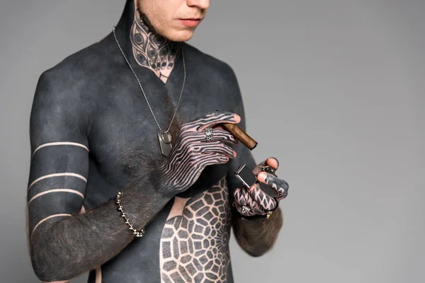 Cropped shot of bare-chested man with tattoos holding cigar and lighter isolated on grey — Stock Photo