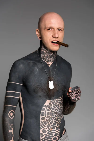 Confident bare-chested man with tattoos smoking cigar and looking at camera isolated on grey — Stock Photo