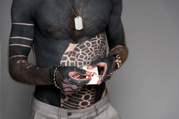 Mid section of bare-chested man with tattoos holding cigarette box isolated on grey — Stock Photo