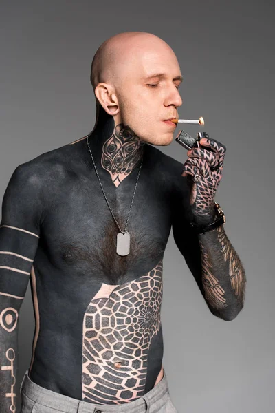 Homme tatoué torse nu allumant cigarette avec briquet isolé sur gris — Photo de stock