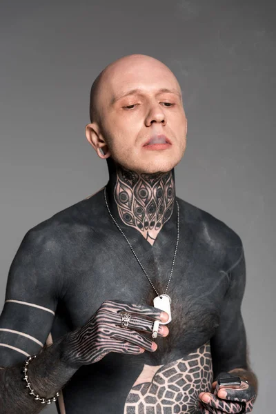 Calvo sin camisa hombre tatuado sosteniendo encendedor y fumar cigarrillo aislado en gris — Stock Photo