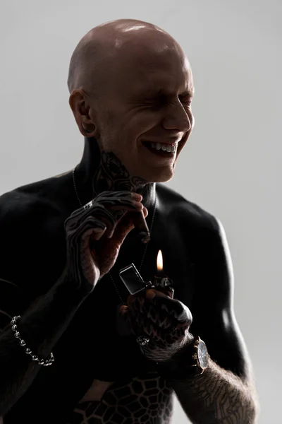 Happy tattooed man holding cigar with lighter and laughing isolated on grey — Stock Photo