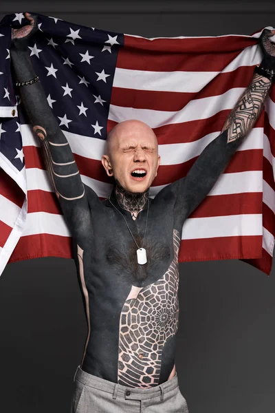 Homme tatoué émotionnel avec les yeux fermés nous tenant drapeau isolé sur gris — Photo de stock