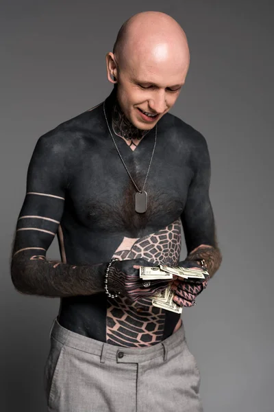 Uomo tatuato sorridente senza maglietta contando banconote in dollari isolate su grigio — Foto stock