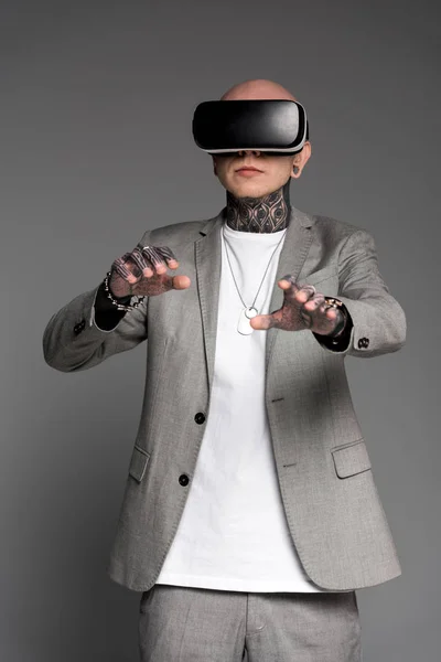 Лисий татуйований чоловік у костюмі з використанням гарнітури віртуальної реальності ізольований на сірому — стокове фото